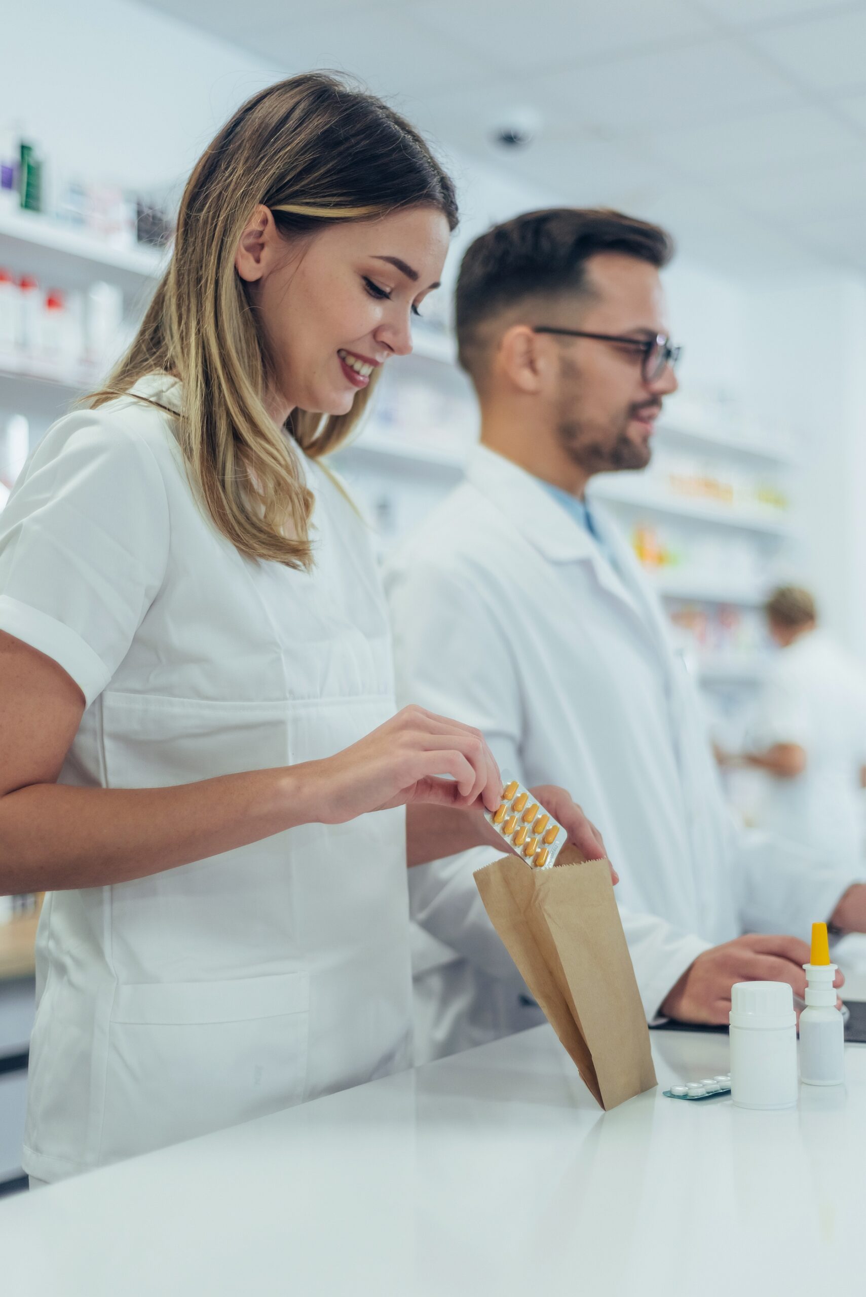 Close shot of a young female pharmacist packing drugs in a paper bag while working in a pharmacy